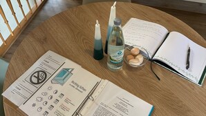 A round wooden table with a notebook, a pen, a candle, and a bottle of water. - Vacation apartment Westerburg for 1-3 persons in Westerburg city center (Westerburg)