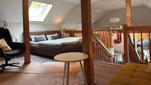 A loft-style bedroom with a skylight, a bed with multiple pillows, a round table, and a staircase. - Vacation apartment Westerburg for 1-3 persons in Westerburg city center (Westerburg)
