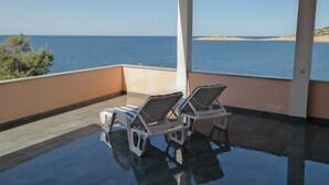 Ein Balkon mit zwei Liegestühlen, Blick auf einen Pool und das Meer.