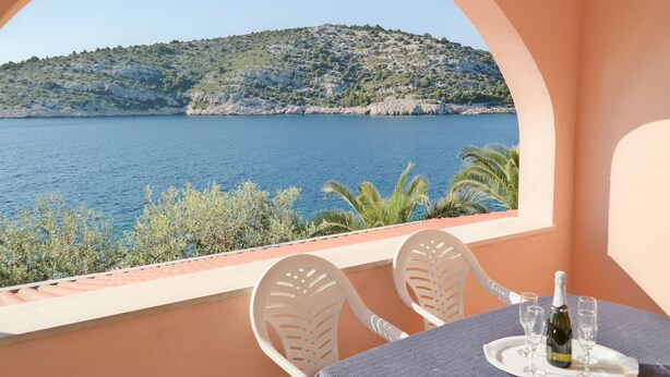 Ein Balkon mit Tisch für zwei Personen, mit Blick auf ein Gewässer und eine hügelige Landschaft.