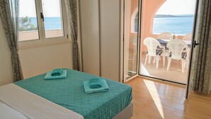 Ein Schlafzimmer mit Bett, Meerblick durch eine Schiebetür und ein Balkon mit Stühlen.