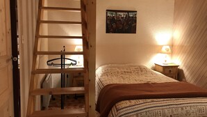 Ein Schlafzimmer mit einer Holzleiter, einem Bett mit gemusterten Bettbezügen, einem Nachttisch mit Lampe und einem an der Wand hängenden Bild.