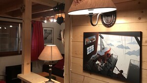 Ein Zimmer mit einer Holzwand, einem Tisch mit Lampe, einem gerahmten Bild und einem Fenster mit rotem Vorhang.