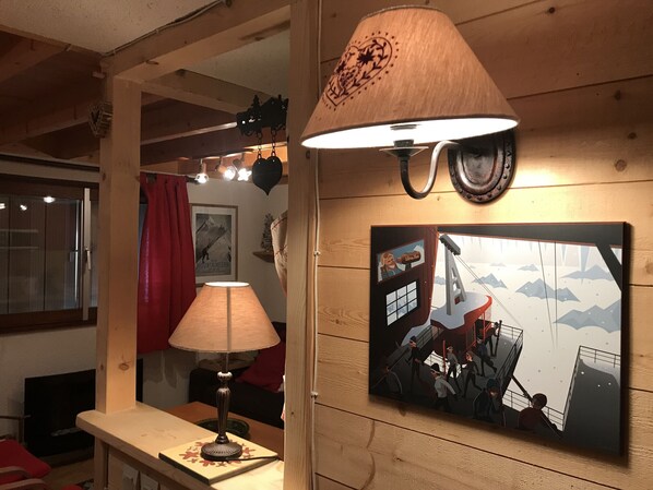 Une pièce avec un mur en bois, une table avec une lampe, un tableau encadré et une fenêtre avec un rideau rouge.