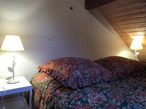 Ein Schlafzimmer mit schrägen Wänden, floralem Bettbezug und Nachttischlampen.