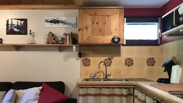 Ein kompakter Wohnbereich mit Küchenzeile, einer Couch mit Kissen, einem Holzschrank und Wanddekoration.