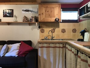 Un espacio habitable compacto con kitchenette, un sofá con cojines, una ventana con cortinas y adornos en la pared.