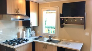 Een compacte keuken met een gasfornuis, een koffiezetapparaat en een raam met uitzicht op groen.