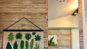 Een wand met een houten paneelmotief, een ingelijste botanische illustratie en een spiegel die een deel van de kamer reflecteert.