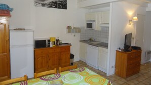 Una cocina compacta con refrigerador, microondas, pileta y gabinetes de madera. En primer plano, una mesa de comedor con mantel colorido.