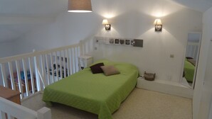 Un dormitorio con una cama verde, paredes blancas, una cuna blanca y dos lámparas fijadas a la pared.