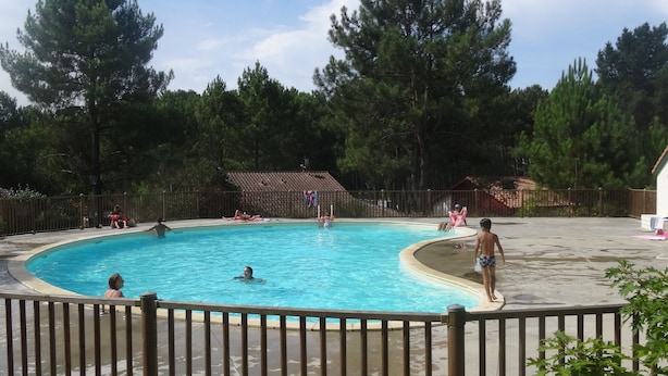 Una piscina rodeada por una cerca de madera, con árboles al fondo.