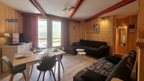 A cozy room with a wooden interior, a dining table with chairs, a sofa, and a television on a dresser. - La Mongie - Apartment T2 for 5 people with balcony - Résidence Béro Bisto (Bagnères-De-Bigorre)
