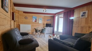 A cozy wooden interior with a sofa, a dining table with chairs, and a television. - La Mongie - Apartment T2 for 5 people with balcony - Résidence Béro Bisto (Bagnères-De-Bigorre)