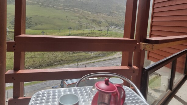 A balcony with a table holding a teapot and cups, overlooking a mountainous landscape with a road and a bridge. - La Mongie - Apartment T2 for 5 people with balcony - Résidence Béro Bisto (Bagnères-De-Bigorre)