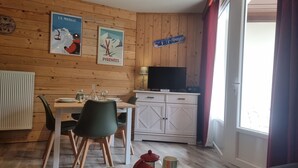 A cozy room with wooden walls, a dining table with chairs, a TV, and a window with curtains. - La Mongie - Apartment T2 for 5 people with balcony - Résidence Béro Bisto (Bagnères-De-Bigorre)