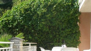 An outdoor patio area with a stone wall, white chairs, and a table set for dining. - Charming 2-Bedroom Apartment for Four, With Parking (Pula)