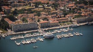 An aerial view of a marina with numerous boats docked, surrounded by historic buildings and a prominent circular structure. - Charming 2-Bedroom Apartment for Four, With Parking (Pula)