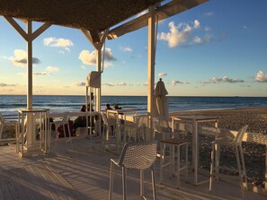 A beachside patio with white chairs and tables, overlooking the ocean.
