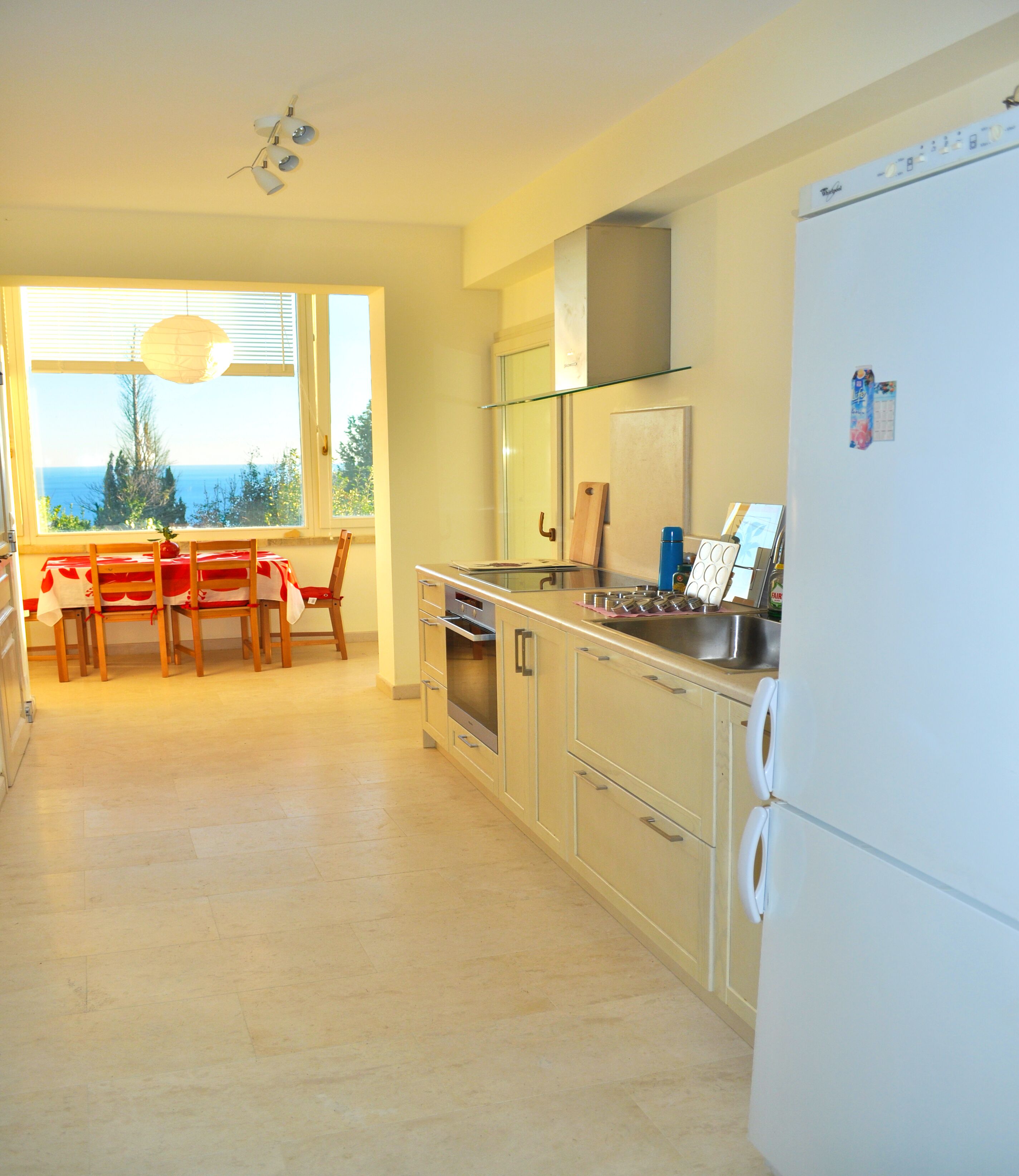 A modern kitchen with a dining area, large windows, and a view of the sea.