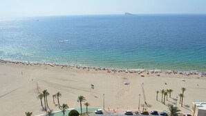 A beach with a clear view of the ocean, palm trees, and a distant island. - Apartment facing the sea. In the center of the Poniente Beach. WIRELESS. Swimming pool (Benidorm)