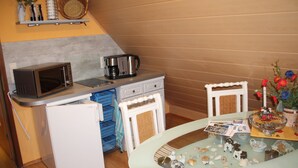 A compact kitchen with a microwave, coffee maker, and a small refrigerator. There is a table with decorative items and a basket.