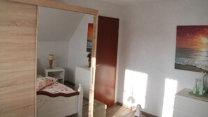 A bedroom with a bed, bedside table, lamp, and a painting of a sunset.