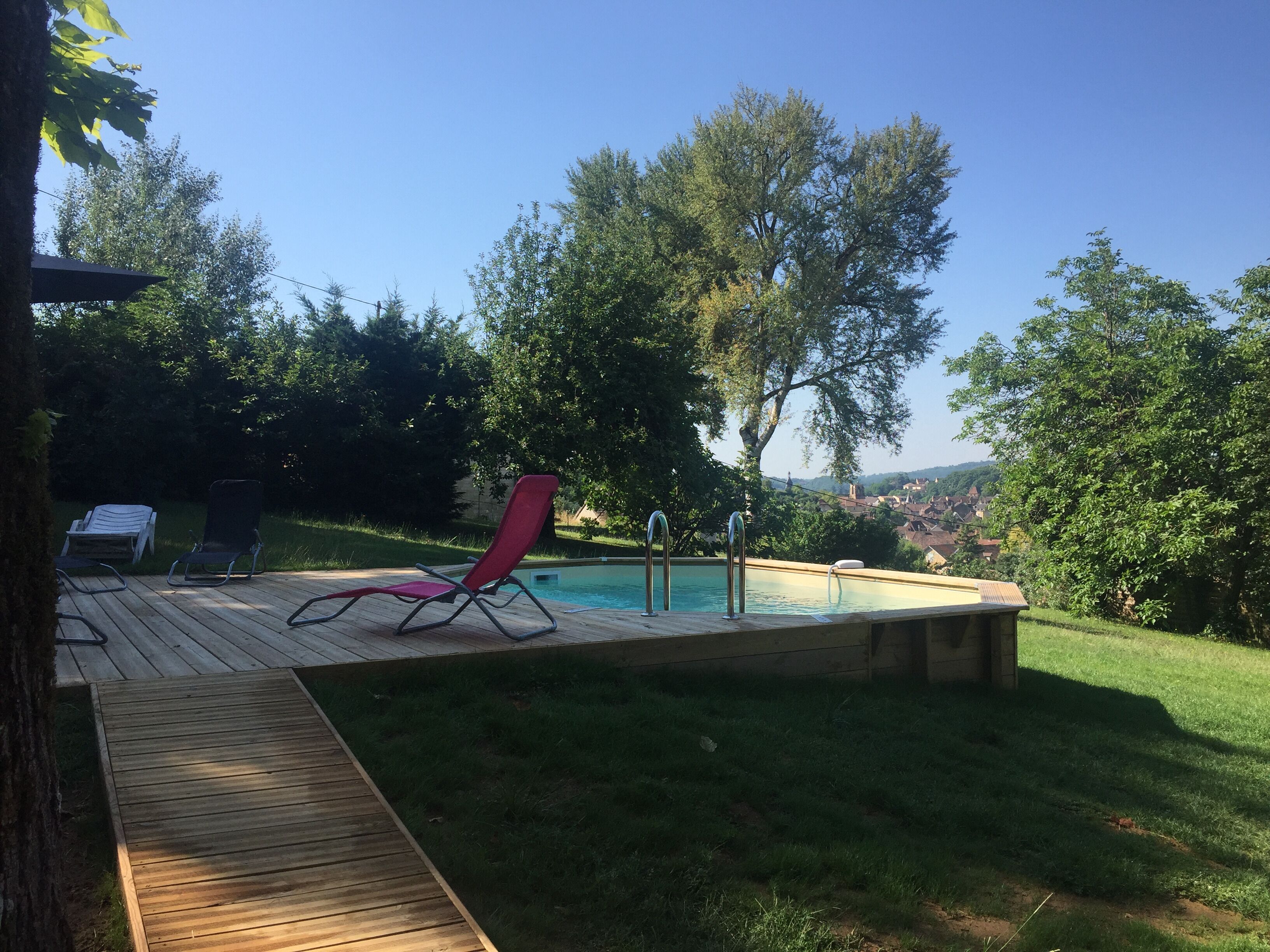 Un patio trasero con piscina, terraza de madera y sillas de descanso.