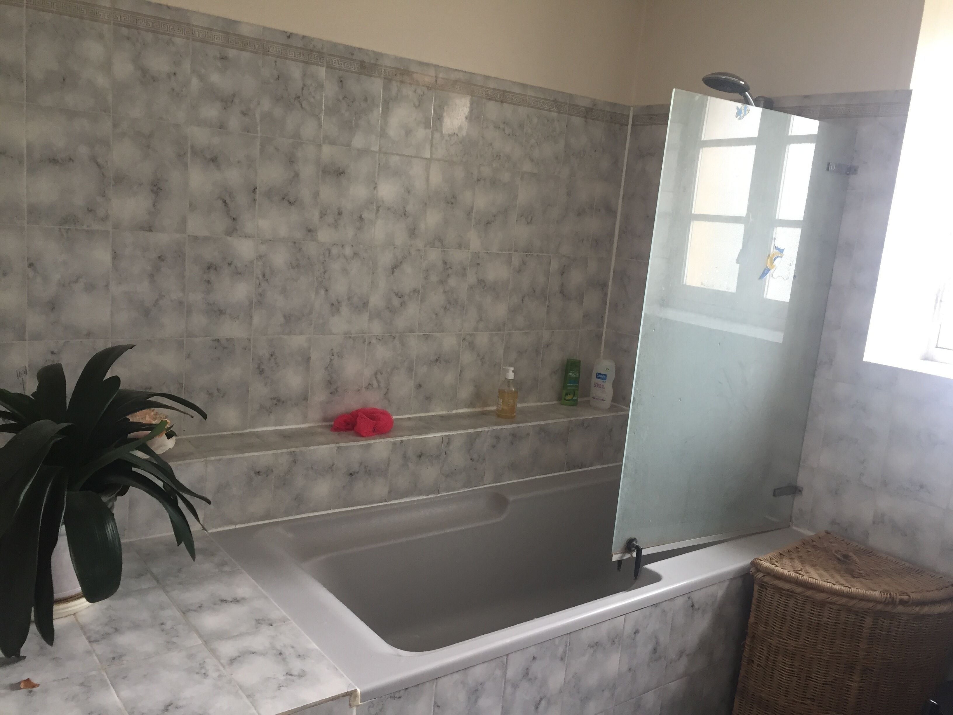A bathroom with a marble-tiled wall, a bathtub, a shower area, and a shelf with toiletries.