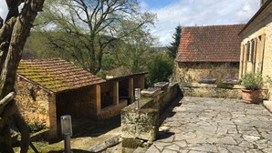 Un patio con pavimento de piedra, un edificio con techo de tejas y un árbol.