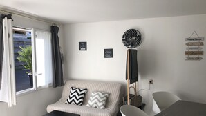 Un salon moderne comprenant un canapé, une table basse, un lampadaire et une table à manger. On y trouve deux éléments de décoration murale et une fenêtre avec des rideaux.