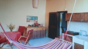 Ein Wohnzimmer mit einer Hängematte, einem Esstisch, Stühlen, einer Küchenzeile und einem Bild an der Wand.