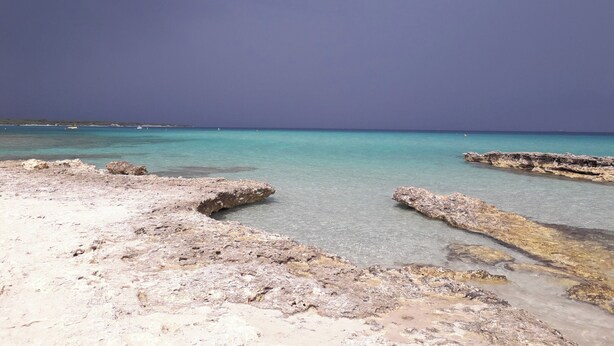 Ein felsiger Strand mit klarem türkisblauem Wasser und einem bewölkten Himmel.