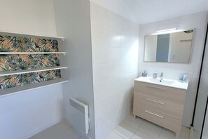 Bathroom features a sink, mirror, and three shelves with tropical leaf-patterned wallpaper.