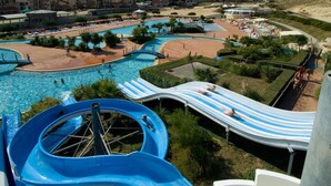 Parque acuático con varias piscinas, un tobogán de agua azul grande y una zona de playa.