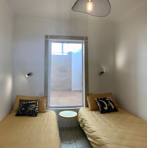 A small, modern room with two beds, a small round table, and a sliding glass door leading to an outdoor area.