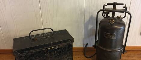 A vintage black metal box with a handle and a metal gas cylinder with a valve and hose.