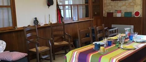 A dining area with a long table set for four, wooden chairs, a colorful tablecloth, and a stone wall with a train sign.