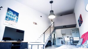 Un salon moderne doté d’un téléviseur à écran plat, d’un escalier et d’un coin cuisine.