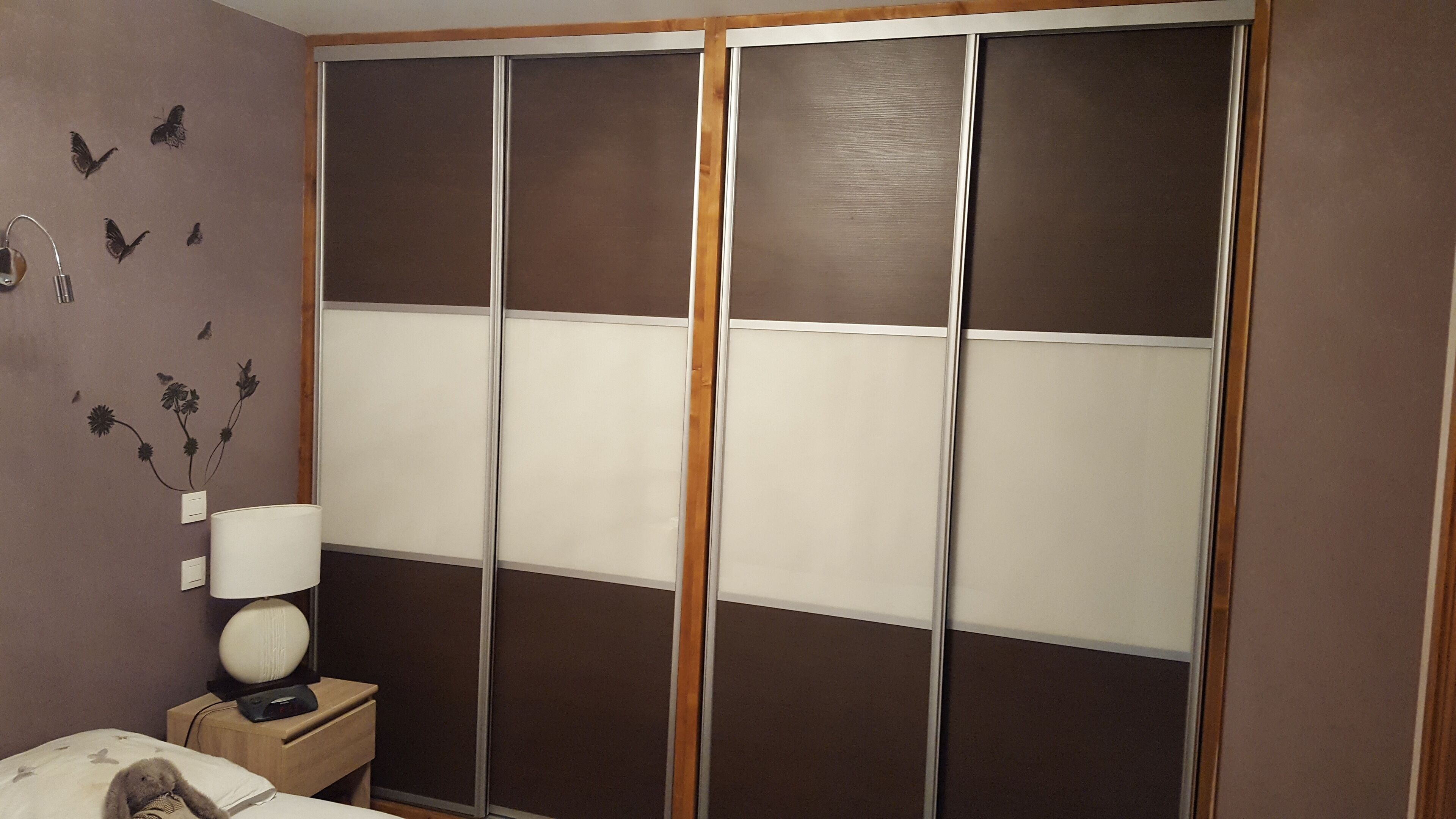A bedroom with a bed, a nightstand, a lamp, and a wardrobe with sliding doors.