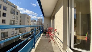 Ein Balkon mit blauer Reling, roten Stühlen und Blick auf benachbarte Gebäude.