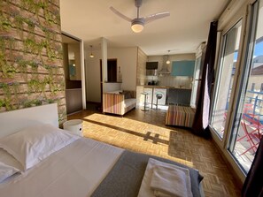 A hotel room with a bed, a small kitchenette, a dining area, and a view of the outside.