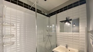 Ein modernes Badezimmer mit einer gläsernen Duschkabine, einem weißen Waschbecken und einem Spiegel darüber.