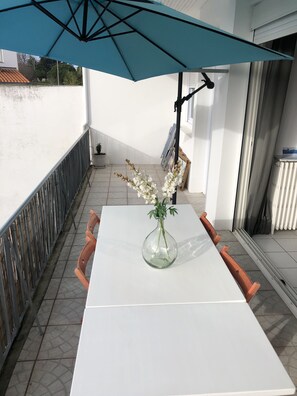 A balcony with a white table, a vase with white flowers, and a blue umbrella. - Charming apartment in Royan, near the beaches and the market. (ROYAN)