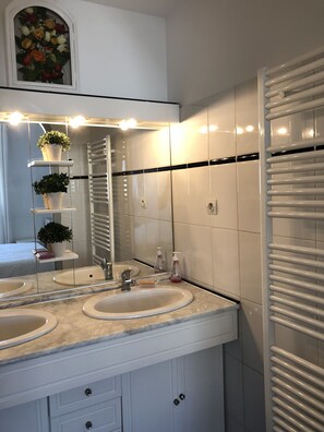 A bathroom with two sinks, a mirror, and a shelf with plants. - Charming apartment in Royan, near the beaches and the market. (ROYAN)