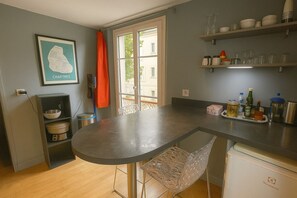 A kitchen with a round table, a chair, a shelf with dishes, and a framed map on the wall.
