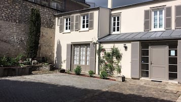 A two-story building with a stone facade, shutters, and a paved courtyard.