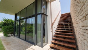 Un edificio moderno con grandes ventanales, una escalera de madera y un muro de piedra.