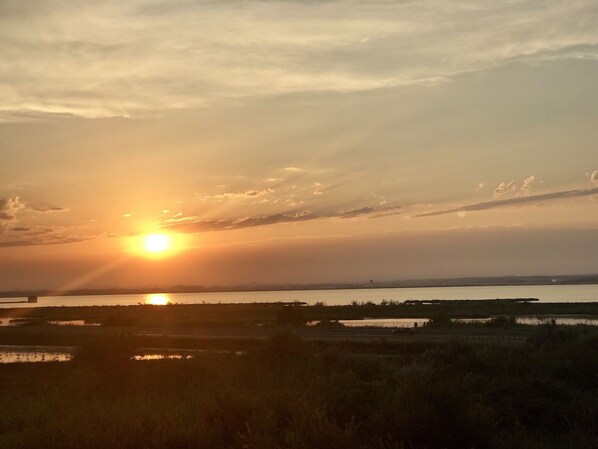 Un coucher de soleil sur un paysage plat, avec des étendues d’eau et un horizon lointain.