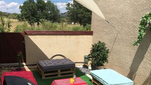 Un patio con césped artificial, una mesa a rayas rojas y blancas, un colchón azul y un banco de madera.